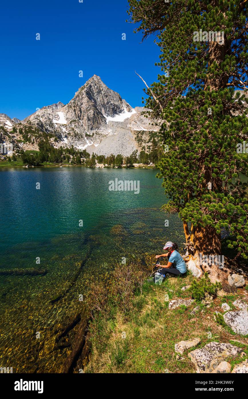 L'escursionista purifica l'acqua sulla riva del lago Treasure, John Muir Wilderness, Sierra Nevada Mountains, California, USA. Foto Stock