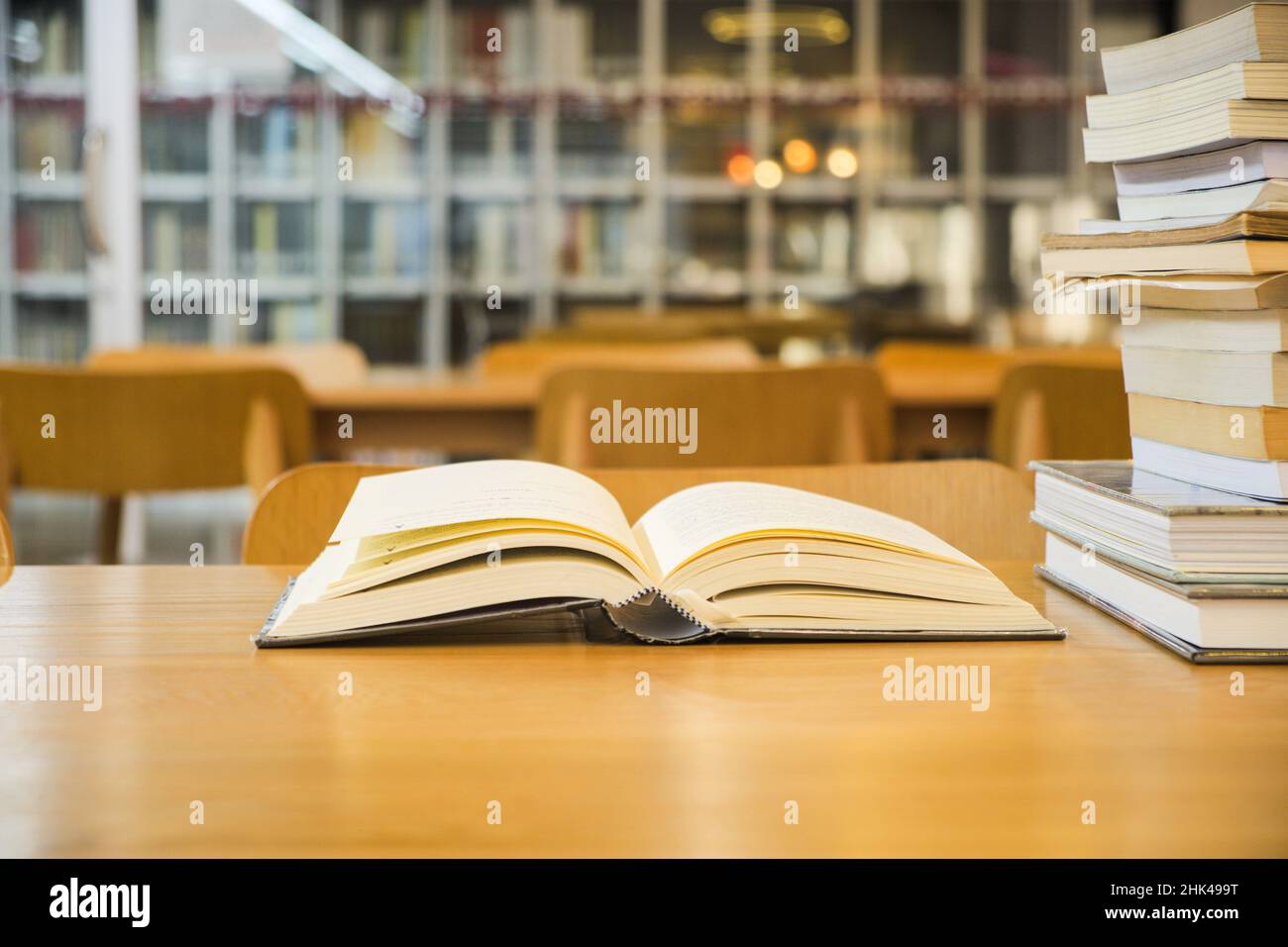 I vecchi libri di testo sono aperti e impilati su un tavolo di legno su una libreria sfocata sullo sfondo della stanza della biblioteca Foto Stock