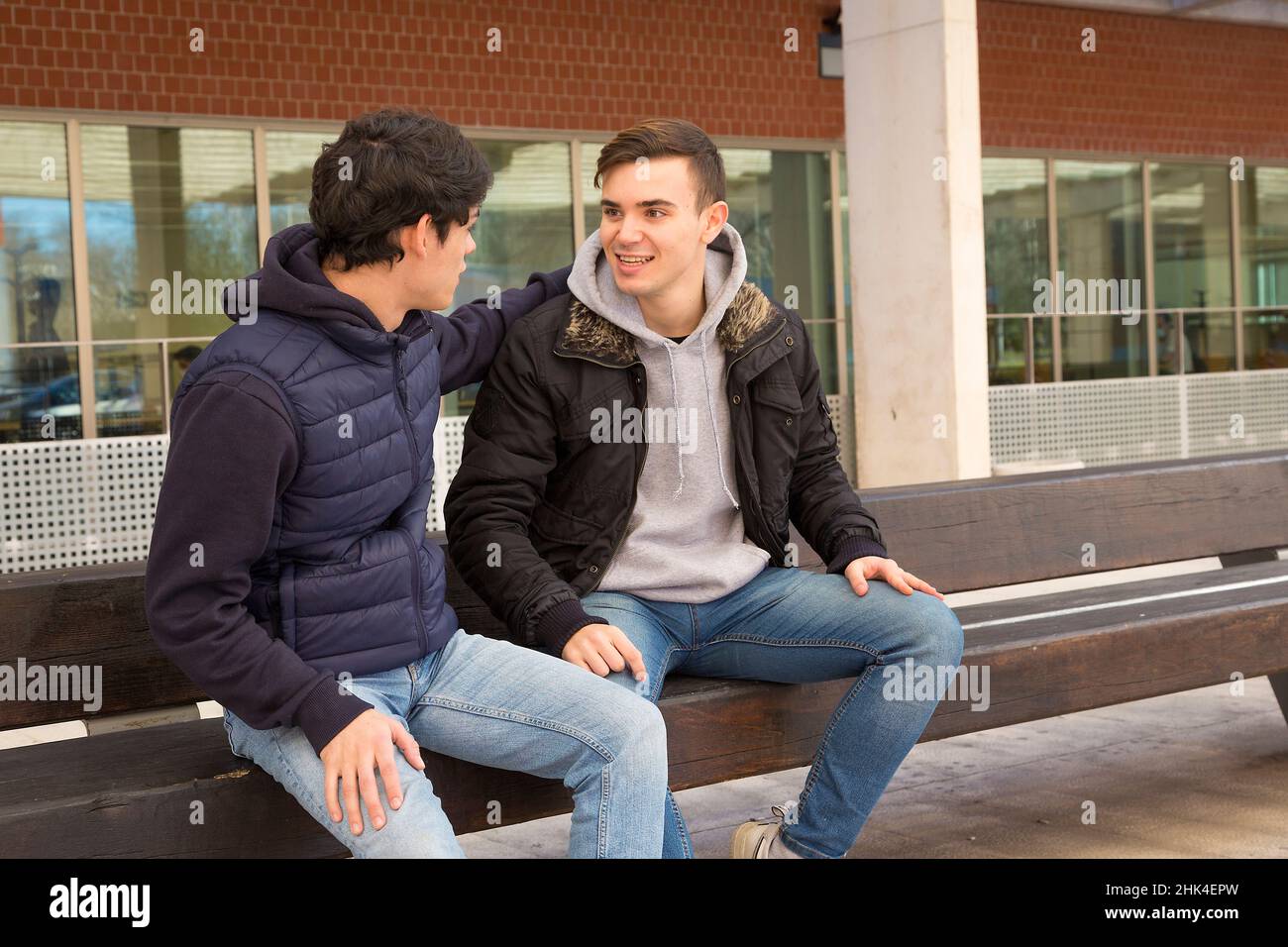 due ragazzi seduti su una panca che parlano Foto Stock