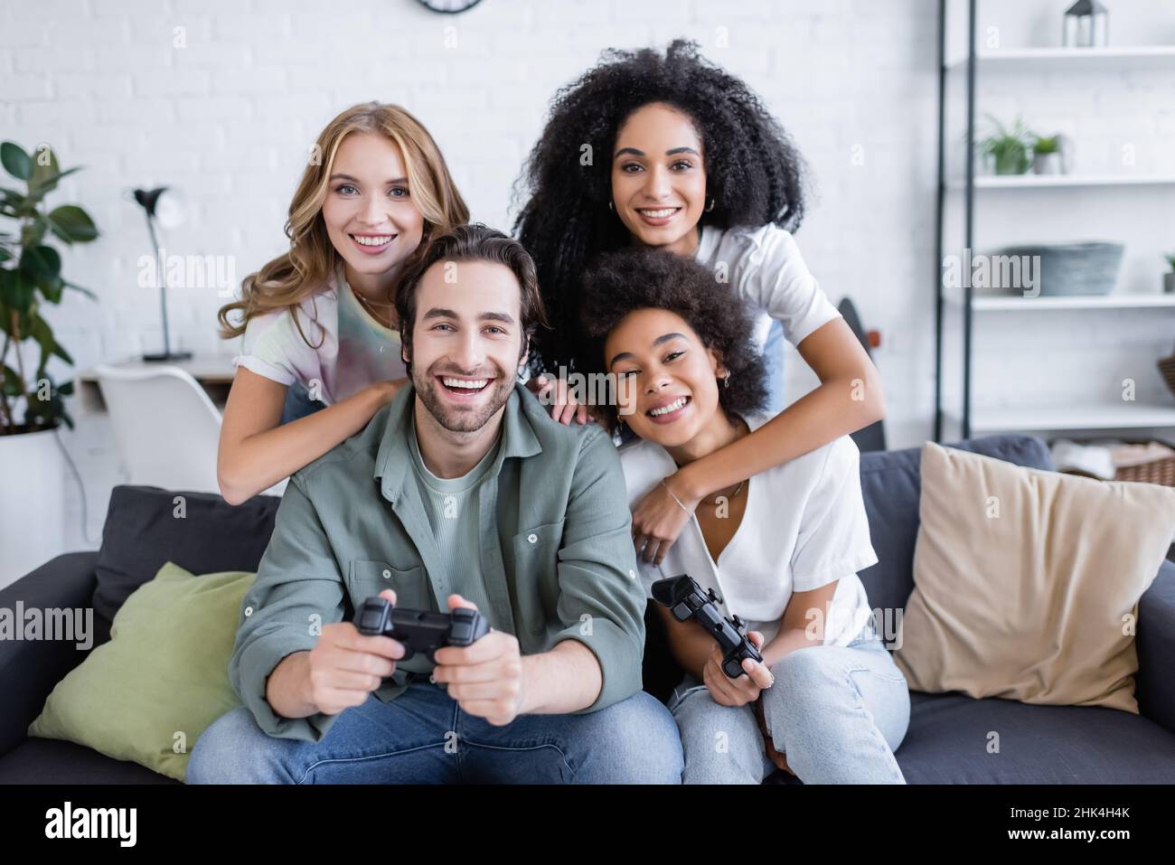 KIEV, UCRAINA - 7 OTTOBRE 2021: Donne polietniche felici che abbracciano gli amici giocando il video gioco in salotto Foto Stock