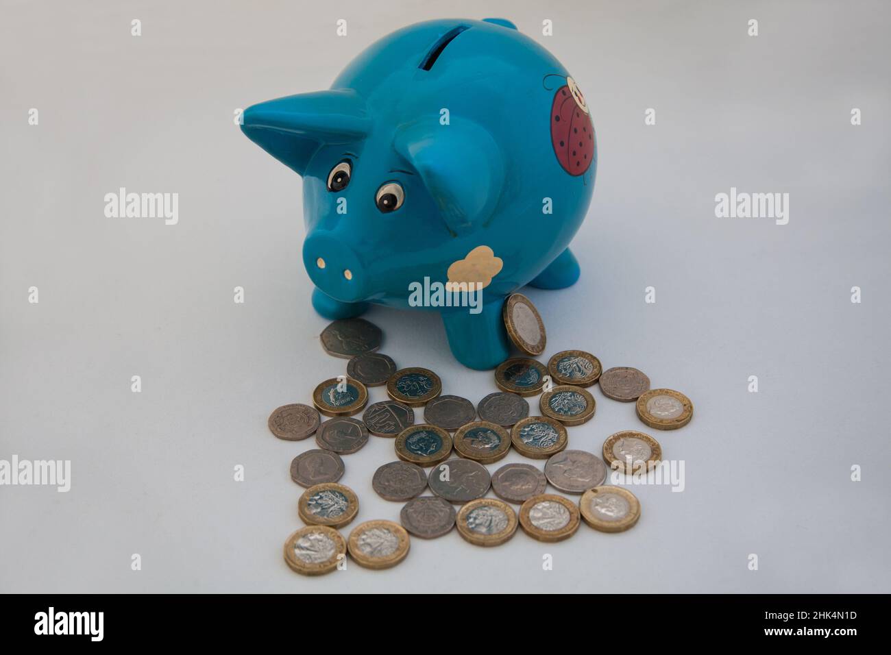 Blue Pig Shaped Piggy Bank con una selezione di monete in sterline britanniche Foto Stock