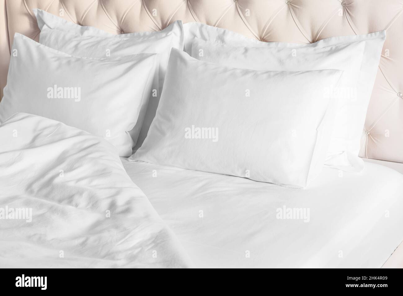 Camera da letto con letto e biancheria da letto bianca cuscini bianchi, piumone e piumone sul letto con testiera beige. Letto con cuscini bianchi e lenzuola pulite Foto Stock
