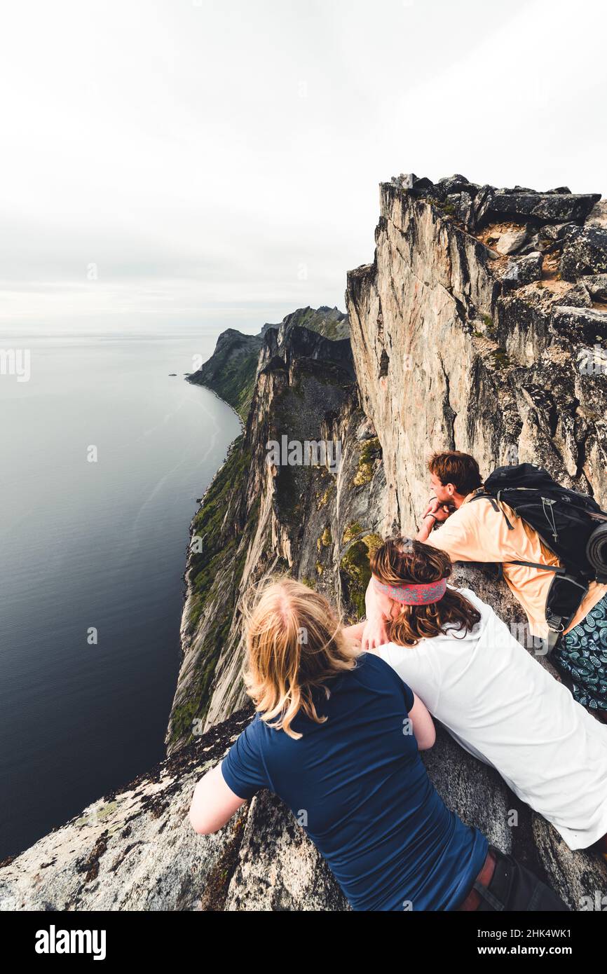 Tre amici che godono la vista del fiordo che si appoggia sulle rocce sulla cima della montagna di Segla, isola di Senja, contea di Troms, Norvegia, Scandinavia, Europa Foto Stock