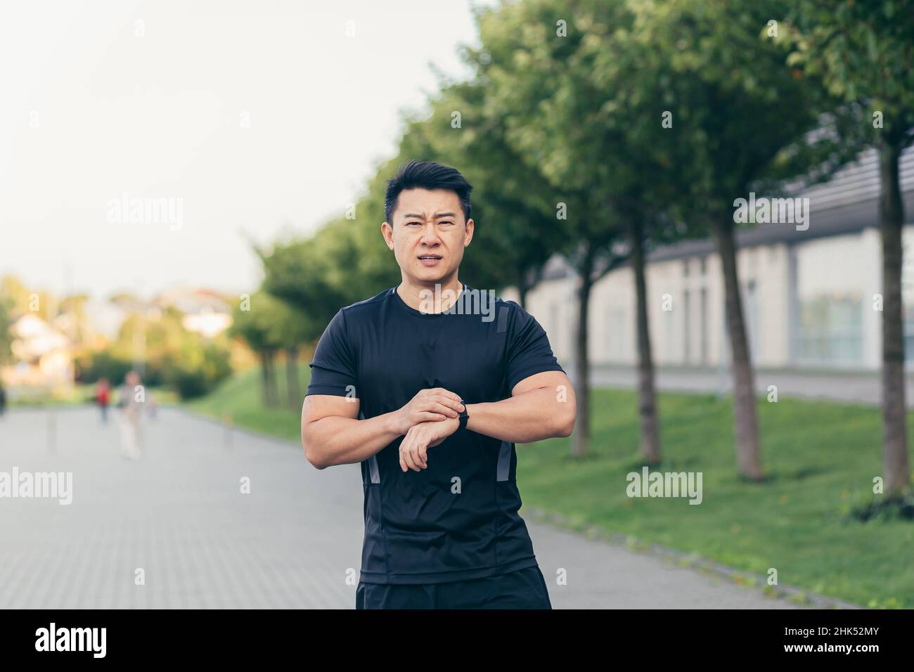 L'atleta asiatico maschile, stanco dopo uno jogging mattutino, corre nel parco vicino allo stadio Foto Stock