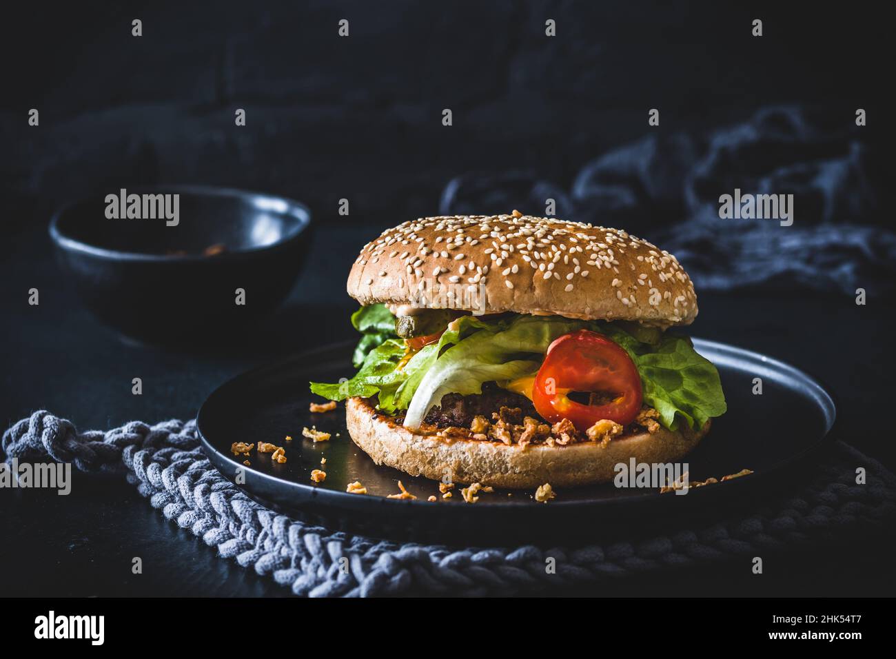 Hamburger al formaggio fatto in casa con cipolle tostate su piastra nera e sfondo nero Foto Stock