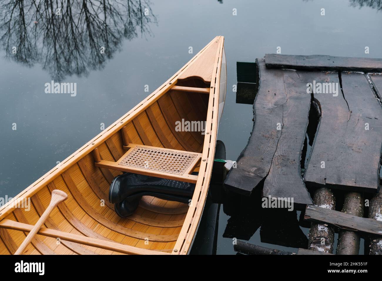 Parte di coda di una canoa in legno sul fiume con stivali di gomma all'interno. Scena naturale autunnale o primaverile, hobby e lifestyle Foto Stock