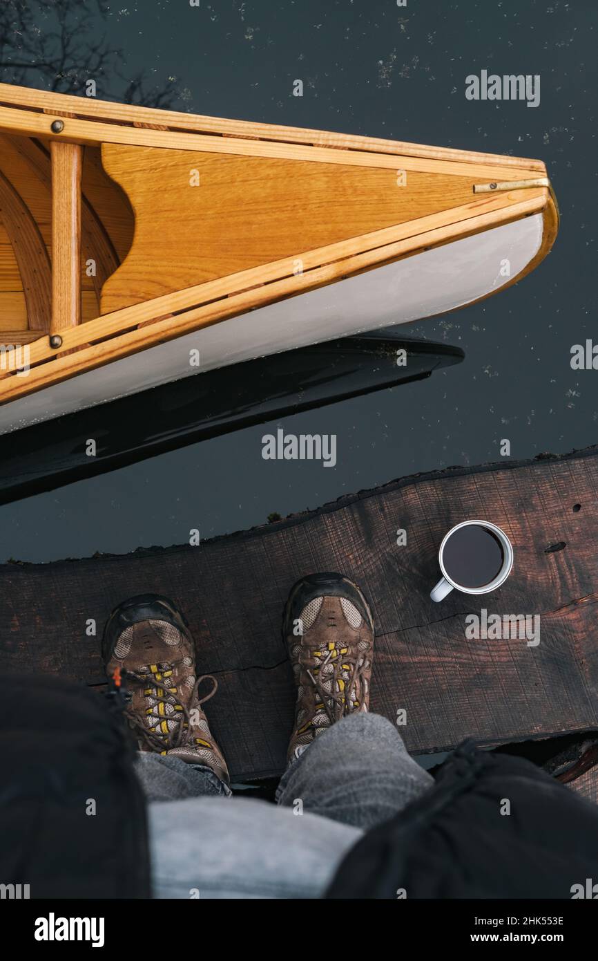 Parte anteriore di una canoa, teglia da caffè e piedi in scarponi da trekking, punto di vista girato. Direttamente sopra la vista di qualcuno in piedi accanto ad una bella Foto Stock