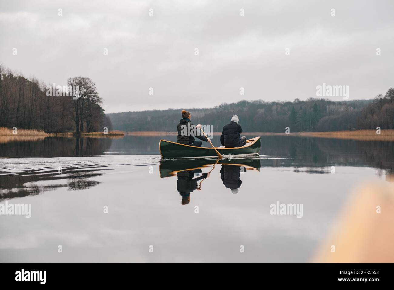 Due uomini pagaiano in canoa canadese sul lago. Stile di vita attivo, una barca di legno sulla superficie di un lago tranquillo foresta in primavera o autunno Foto Stock