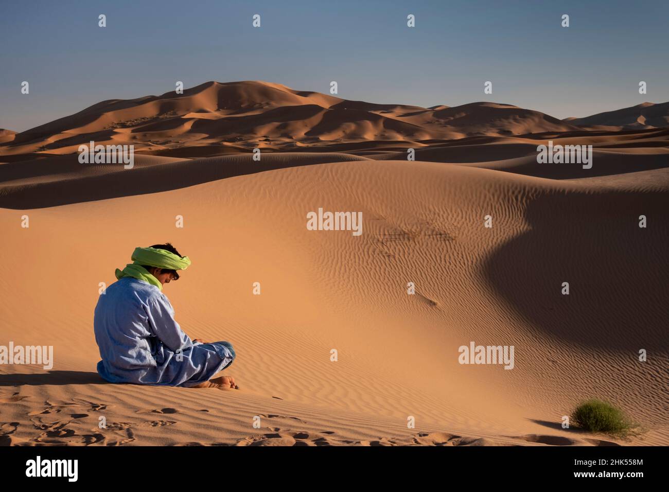 Un uomo berbero in abito tradizionale siede tra le dune di sabbia di Erg Chebbi, deserto del Sahara, Marocco, Nord Africa, Africa Foto Stock