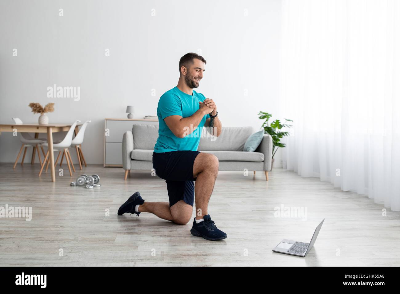 Sorridendo giovane uomo caucasico muscolare facendo esercizi sulle gambe e guardando la lezione online sul computer Foto Stock