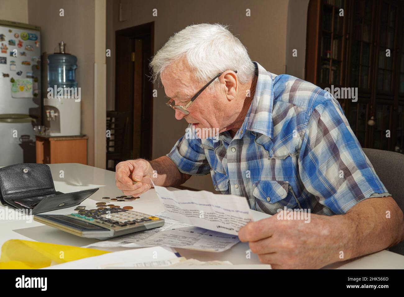 Uomo anziano seduto al tavolo e calcolando le finanze. Vecchio controllo fatture. Uomo che conta le monete sul tavolo. Concetto di calcolo della pensione Foto Stock