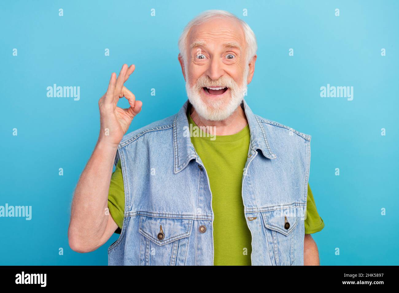 Foto di carino eccitato uomo in pensione indossare vintage jeans gilet  mostrando okey sorridente isolato sfondo di colore blu Foto stock - Alamy
