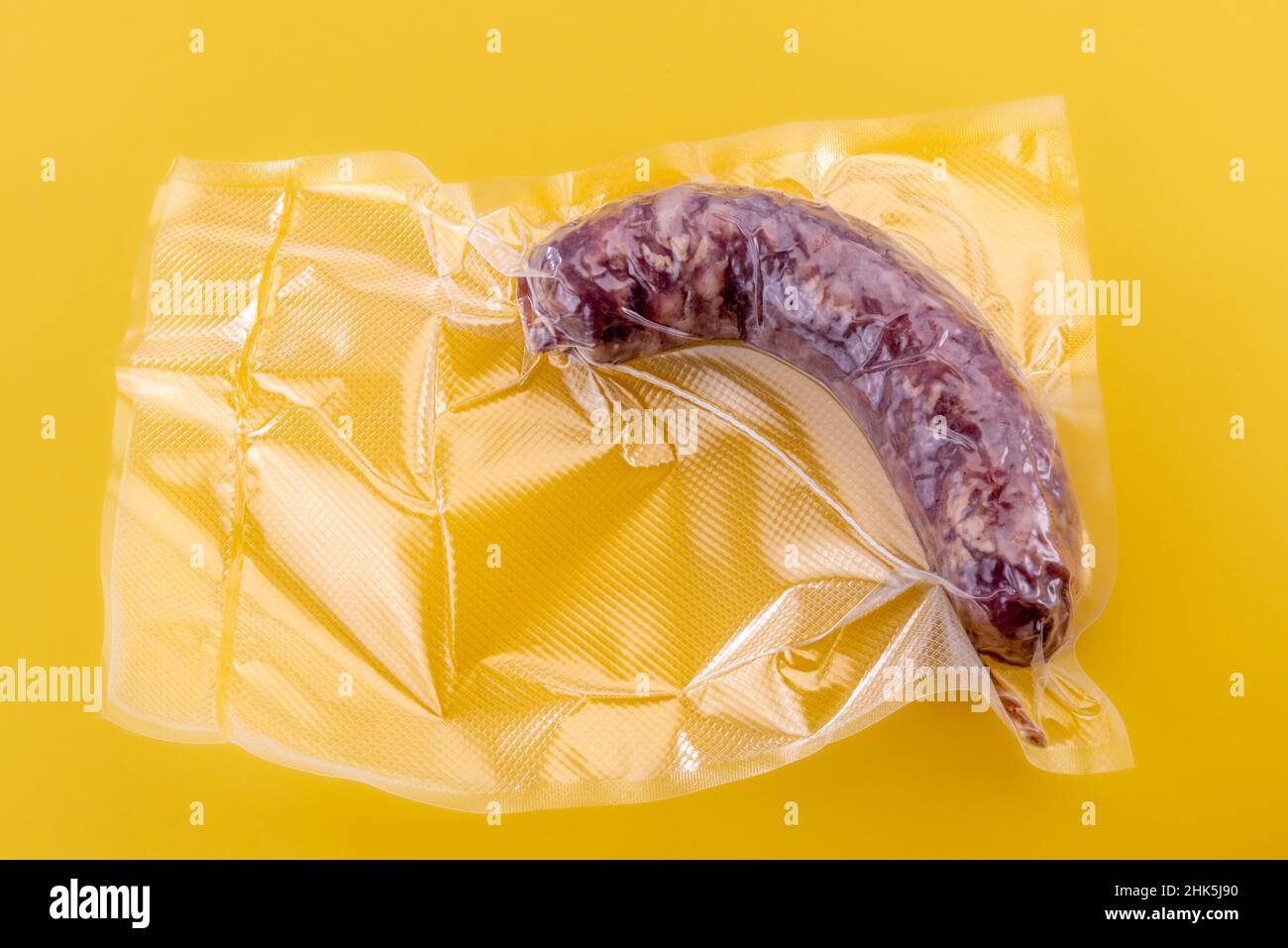 Salsiccia di salame italiana confezionata sottovuoto sigillata per la cottura sous vide isolata su sfondo giallo in vista dall'alto Foto Stock