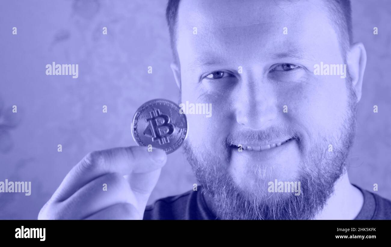 Ritratto di un ricco portatore che tiene in mano una moneta di bitcoin d'oro. Il concetto di estrazione mineraria, criptovaluta, estrazione mineraria e insediamento con elettronica Foto Stock