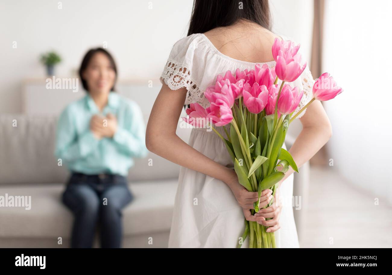 Piccola ragazza asiatica che nasconde fiori per la sua nonna felice dietro, rendendo la vacanza sorpresa a casa Foto Stock