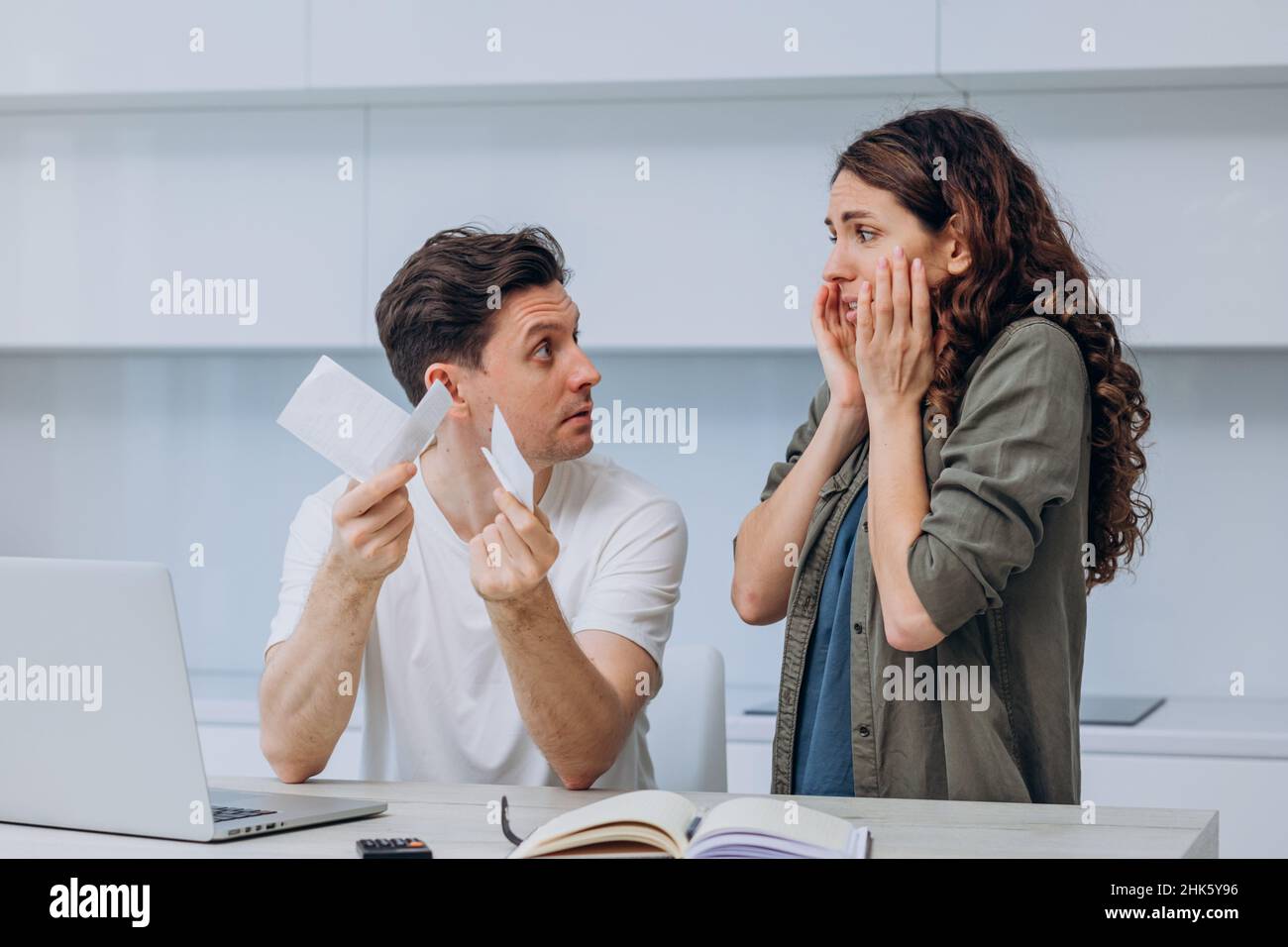 Coppia della moglie di brunette e del marito scuro-capelli che tiene il controllo del supermercato sostiene gesturing circa le spese non pianificate della famiglia dopo il calcolo Foto Stock