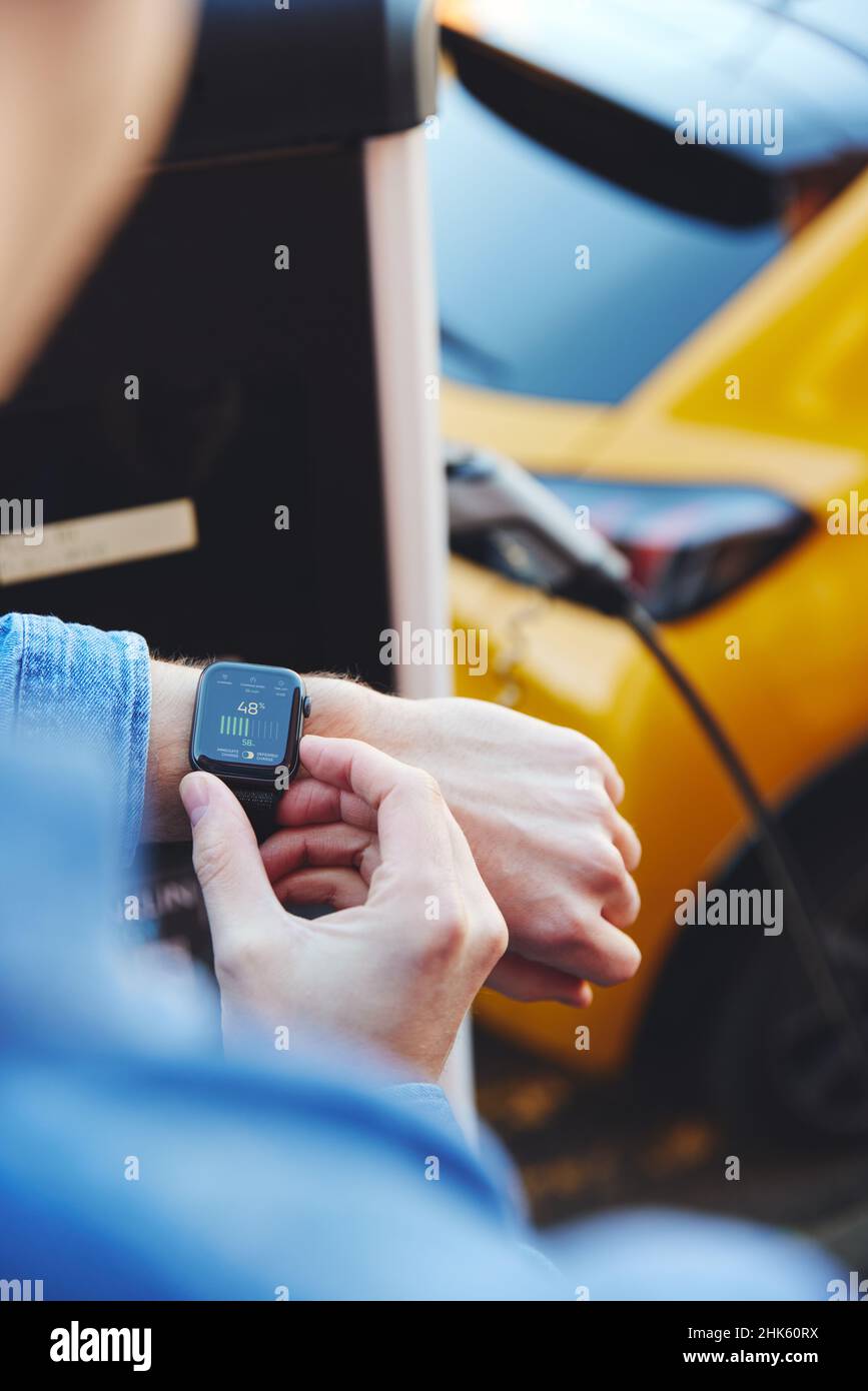 Uomo di carica del veicolo elettrico con cavo Guardando App su Smart Watch Foto Stock