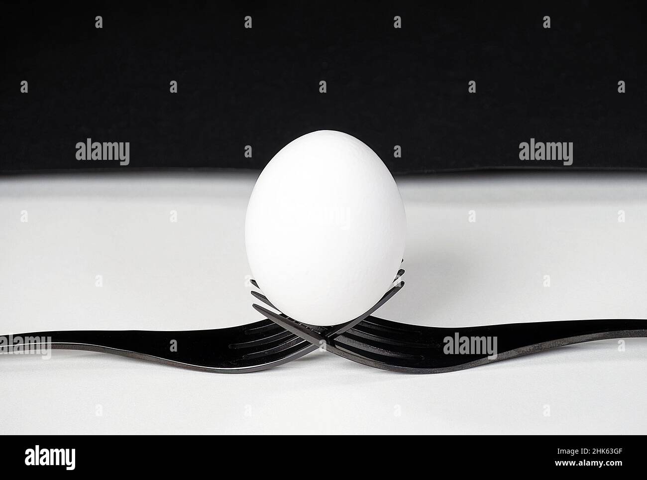 Primo piano di un uovo bianco che si bilancia su un paio di forcelle nere su bianco Foto Stock