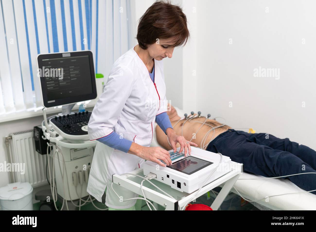 Il medico cardiologo esegue una procedura di elettrocardiografia su un uomo che si trova sul lettino dell'ospedale. Test ECG di sesso maschile in clinica moderna. Diagnostica, healthcar Foto Stock