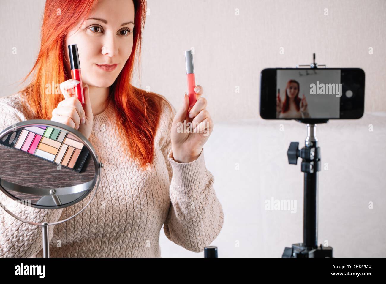 Giovane blogger di bellezza donna dai capelli rossi sta registrando contenuti video per vlog. Influencer mostra come utilizzare cosmetici e trucco. Donna d'affari moderna wor Foto Stock
