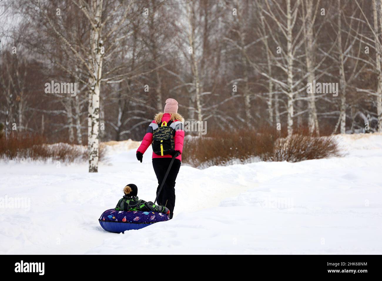 Donna corre un bambino su neve tube, famiglia tempo libero nel parco invernale Foto Stock