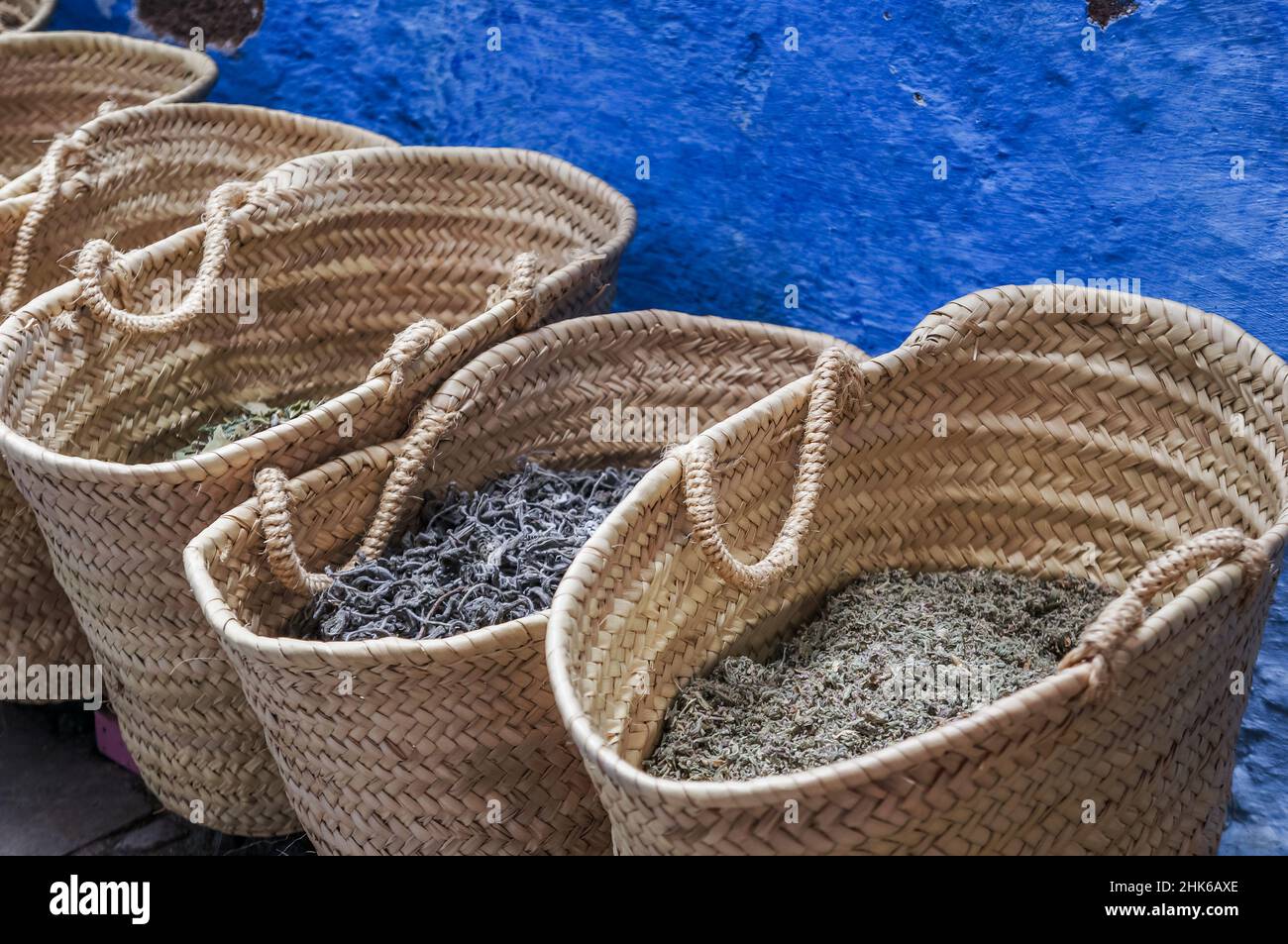 Una fila di cesti di vimini con erbe contro un muro blu in un mercato marocchino Foto Stock