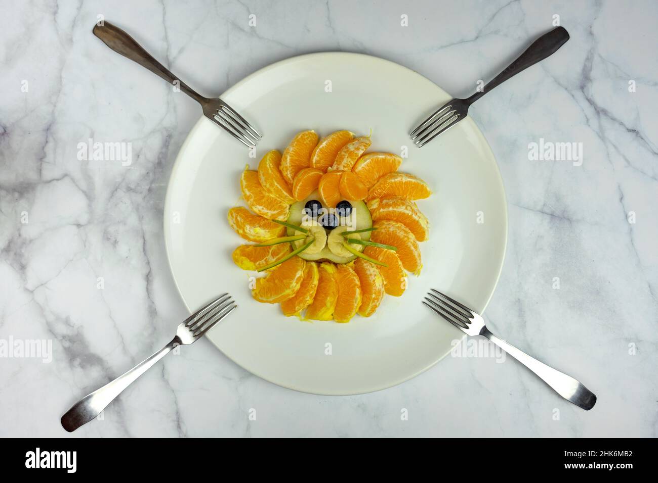 divertente composizione del viso del leone con frutti come il mirtillo d'arancio su un tavolo di marmo con forcelle Foto Stock