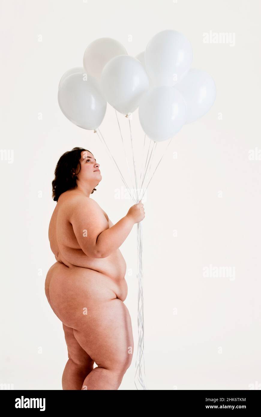 Donna nuda sovrappeso che tiene in su i palloncini bianchi Foto Stock