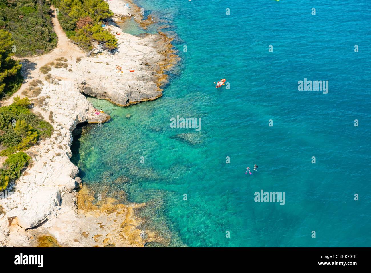 Vista dall'alto di sportivi o turisti in kayak nelle acque turchesi blu trasparente della costa rocciosa del mare Adriatico. Attività di svago estiva in canoa. Foto Stock