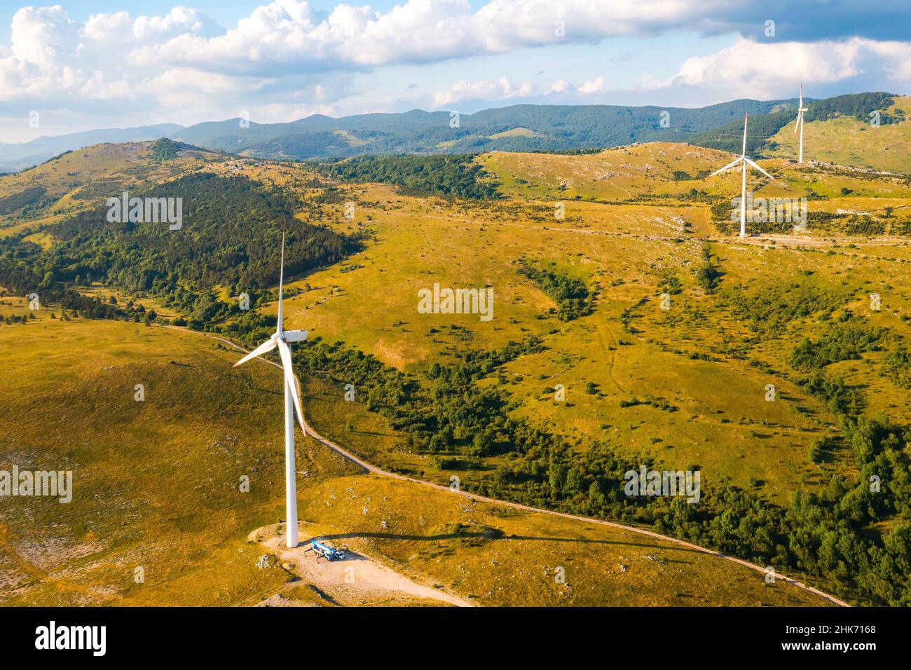 La stazione eolica con potenti macchine che producono energia pulita opera su pendii ricoperti di foreste e cespugli sotto la vista aerea del cielo nuvoloso Foto Stock