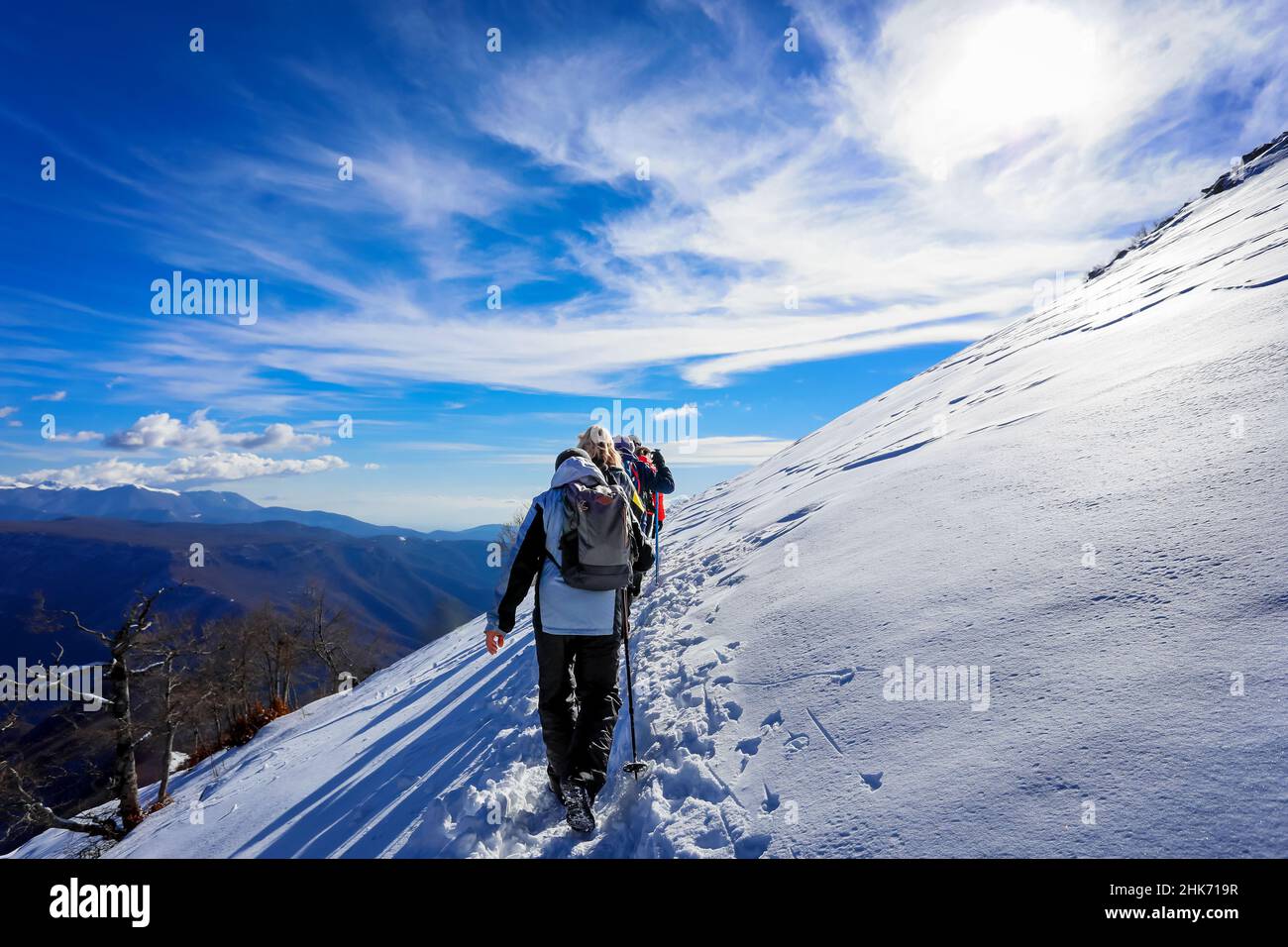 Gruppo di escursionisti di montagna in file unico salire la cima nevosa. Sullo sfondo il cielo blu nuvoloso. Foto Stock