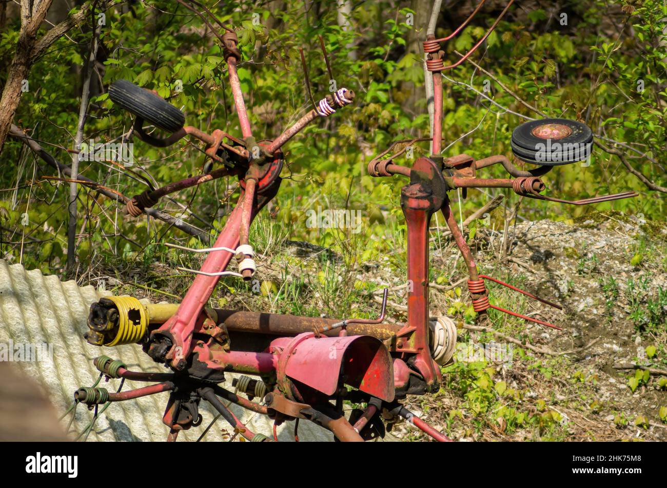 Un vecchio pezzo arrugginito di attrezzature agricole, un tedder sul bordo di una zona boschiva. Foto Stock