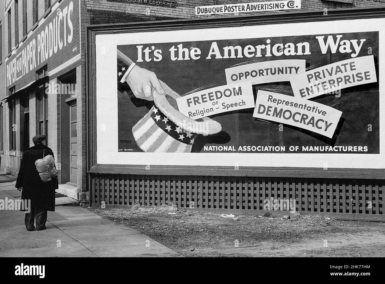 STILE DI VITA "AMERICAN WAY" CONTRASTA USA Rich & Poor Archive 1940s American Contrasts in Lifestyle 'ITS The American Way' National Association of Manufacturers signboard, con Down on His Luck man Passing in Dubuque, Iowa, USA aprile 1940 Foto Stock