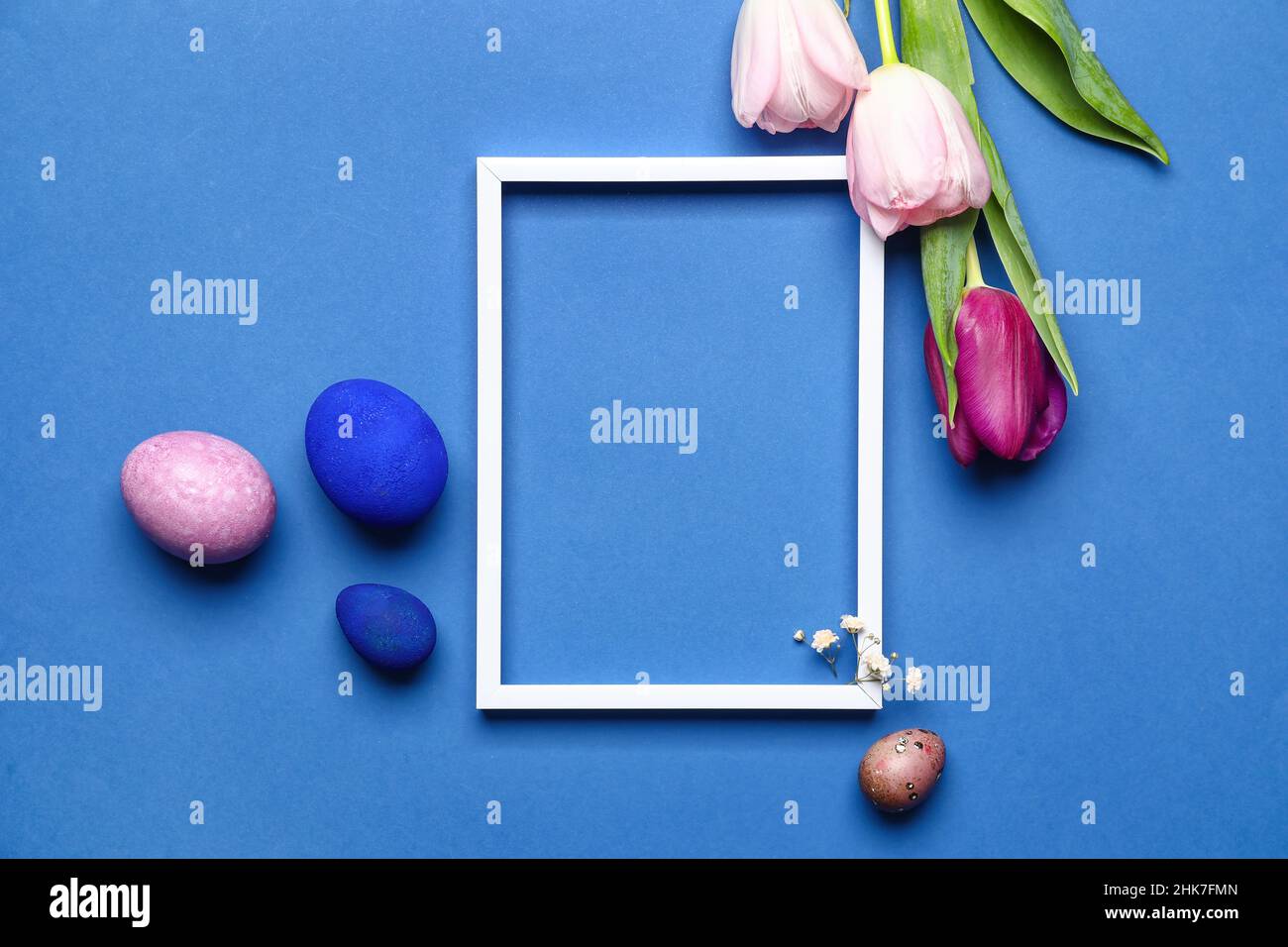 Composizione pasquale con cornice bianca, uova e fiori su sfondo blu Foto Stock