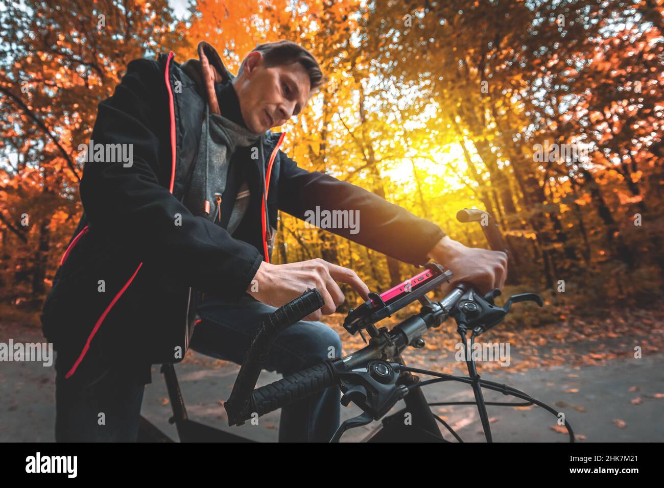 Un uomo in bicicletta utilizza un telefono sul volante in una foresta d'autunno la sera al tramonto Foto Stock