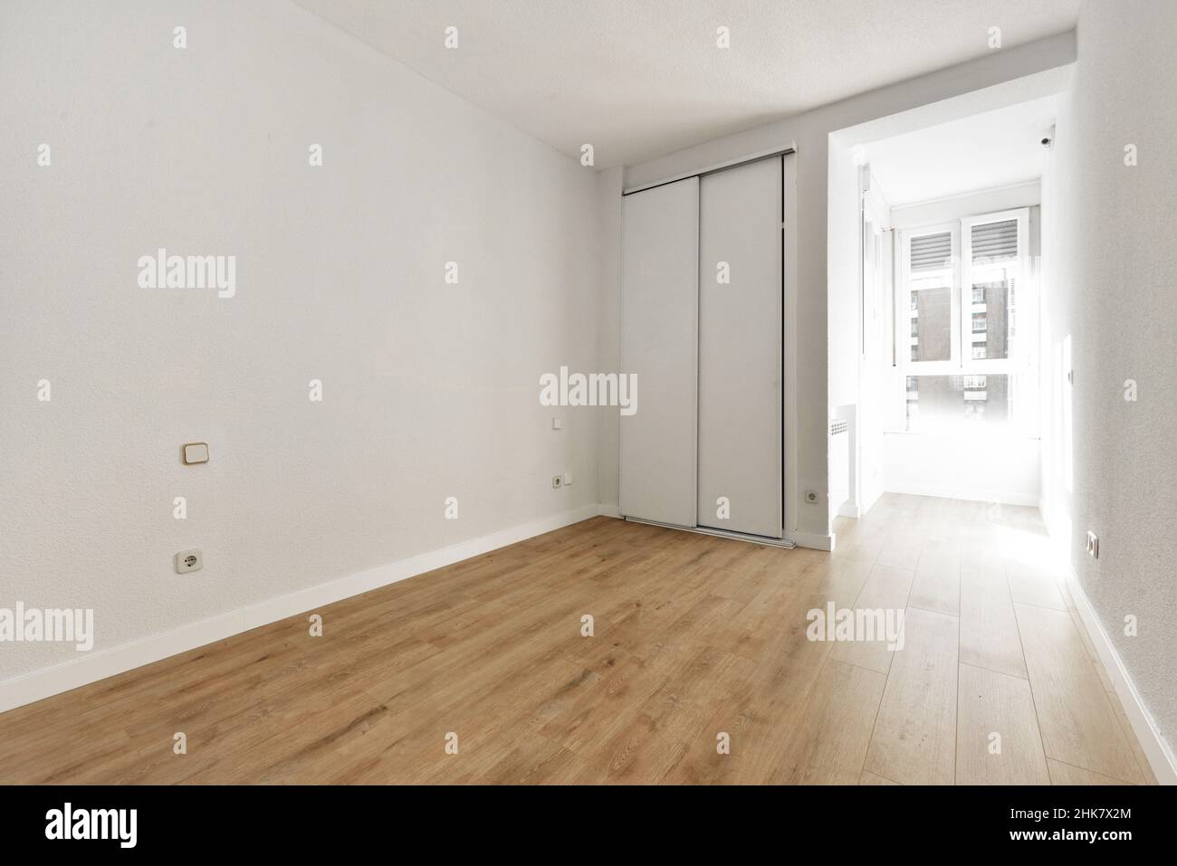 Camera vuota con armadio a muro con porte scorrevoli e finestra bianca attraverso la quale entra molta luce Foto Stock