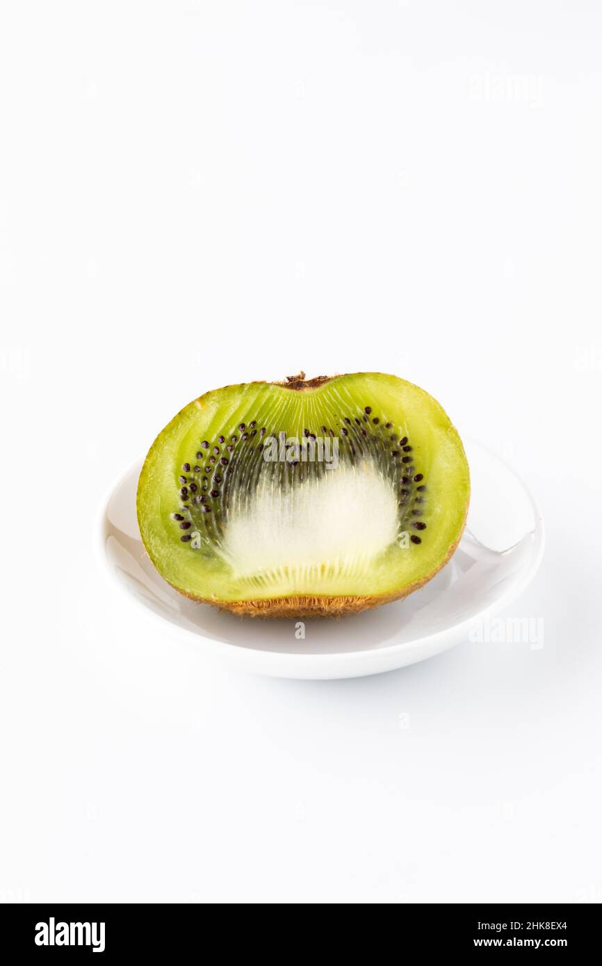 Un kiwi tagliato su un piccolo piatto isolato su uno sfondo bianco. Foto Stock