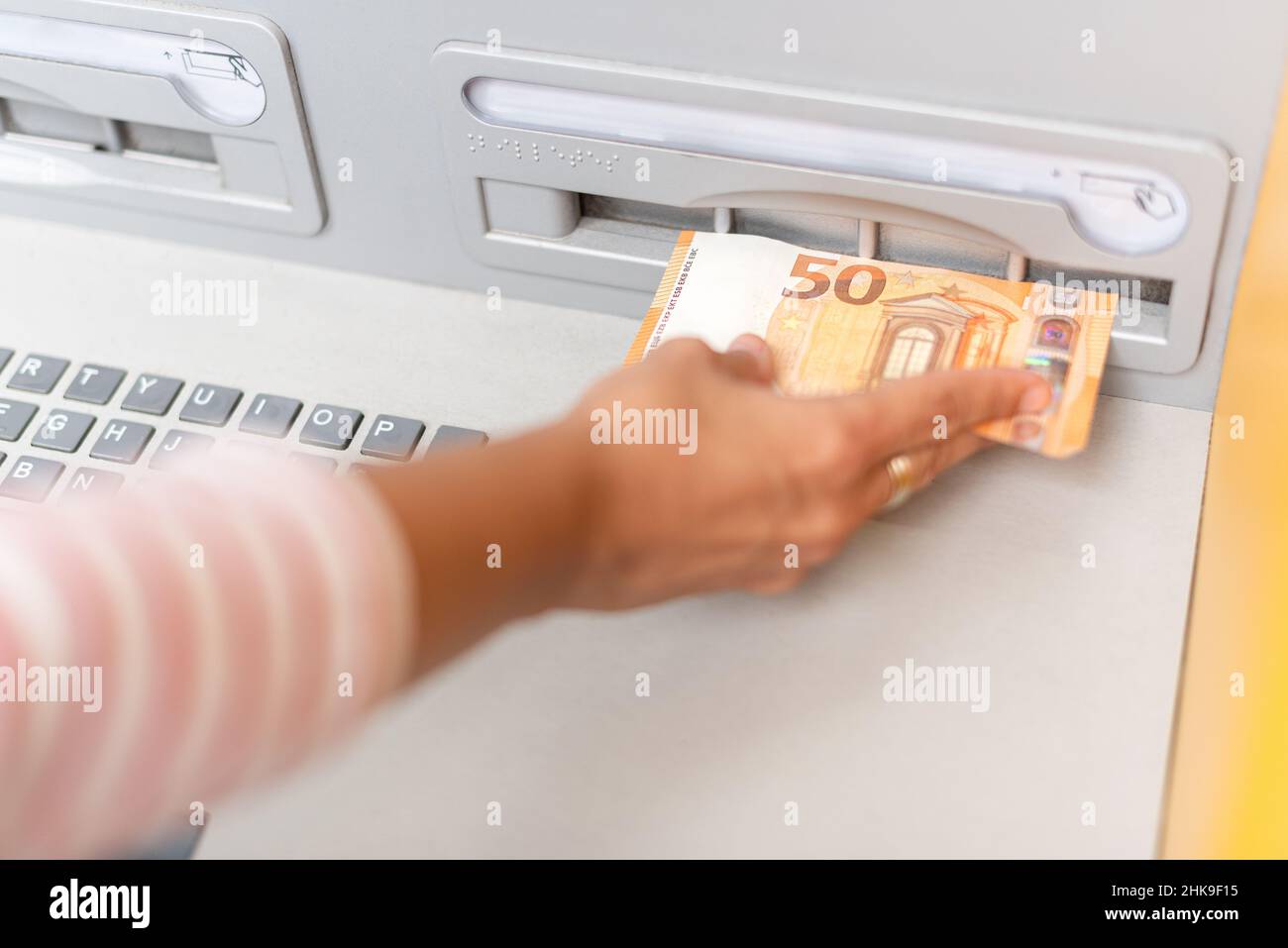Donna di raccolto che mette i soldi sulla carta in ATM Foto Stock