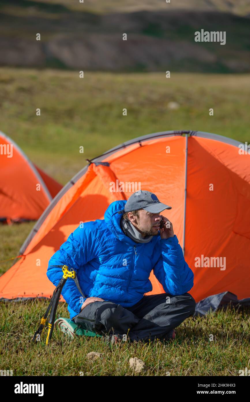 Uomo seduto dopo un'escursione in montagna nel campo e parlare al telefono satellitare Foto Stock