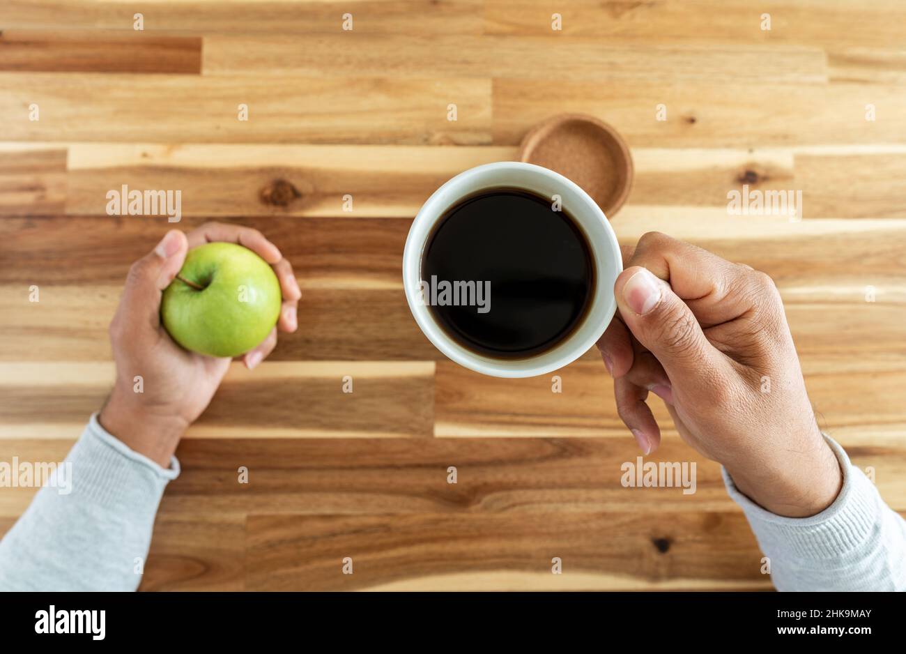 Foto dall'alto dell'uomo che tiene la tazza di caffè e la mela. Concetto di dipendenza della caffeina Foto Stock