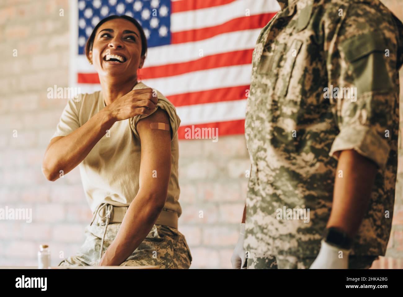 Gli Stati Uniti sorridevano felicemente dopo essere stati vaccinati nella clinica militare. Ragazza allegra soldato che tira giù la manica dopo la recita Foto Stock