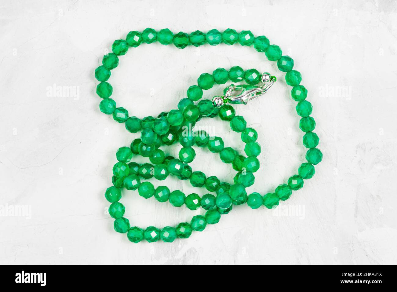 collana artigianale aggrovigliata con perline di agata color verde smeraldo su asse di cemento grigio Foto Stock