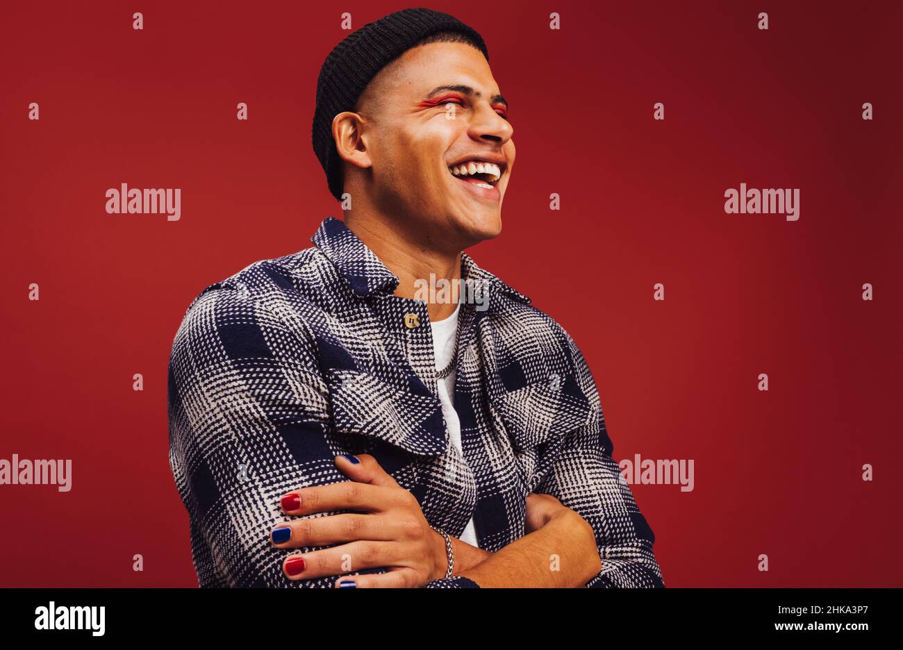 Spensierate il giovane sorridendo con gli occhi chiusi in uno studio. Felice giovane uomo in piedi da solo su sfondo rosso. Giovane uomo alla moda che indossa na Foto Stock