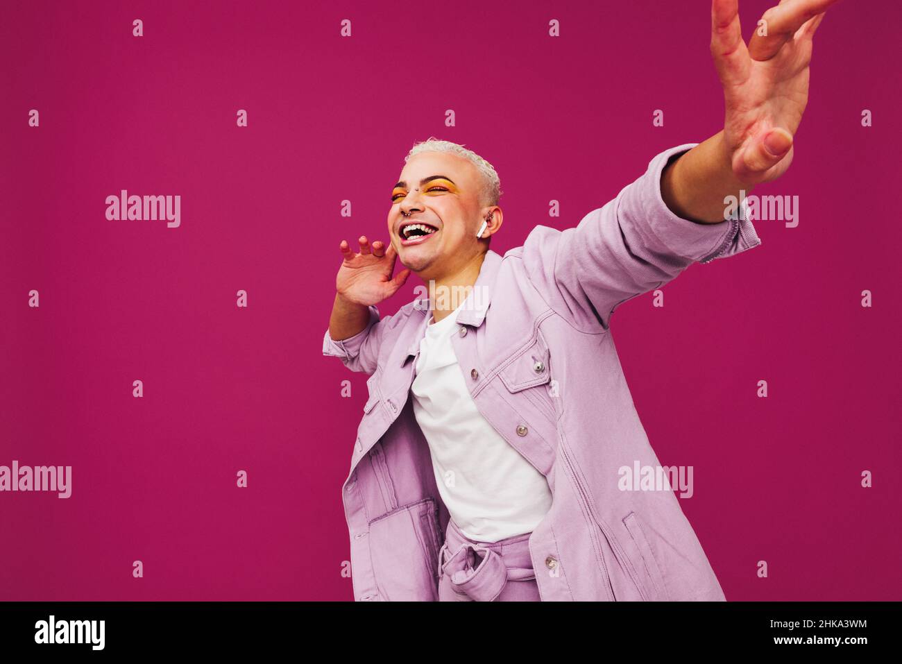 Hipster godendo la sua musica preferita. Non conforme queer man ballare allegro mentre si ascolta la musica su auricolari wireless. Sorridente giovane uomo st Foto Stock