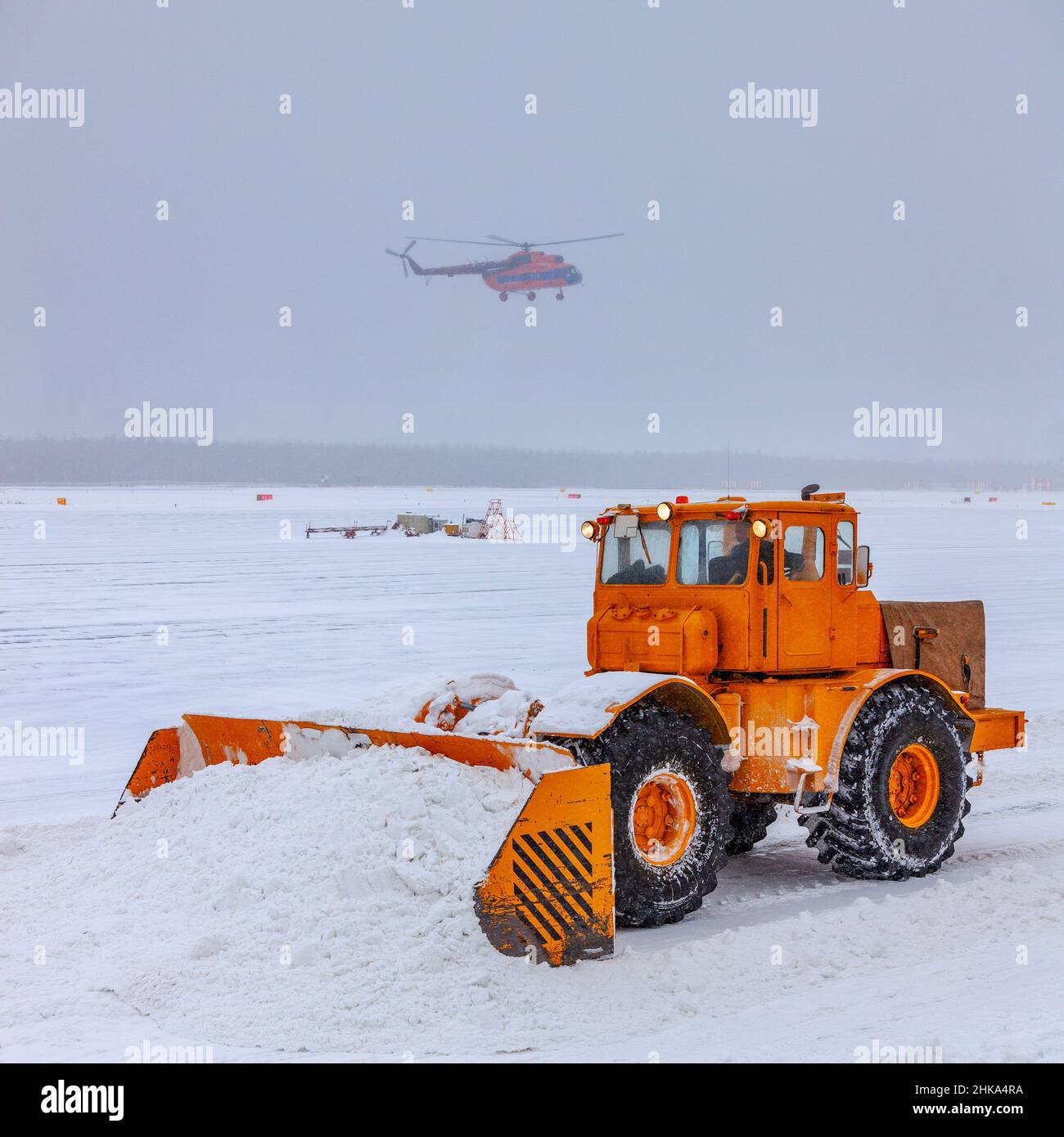 L'aratro da neve pulisce la pista dopo una forte tempesta di neve. L'elicottero sta atterrando in cattive condizioni meteorologiche, durante una nevicata pesante. Foto Stock L'aratro da neve pulisce la pista dopo una forte tempesta di neve. L'elicottero sta atterrando in cattive condizioni meteorologiche, durante una nevicata pesante. Foto Stock