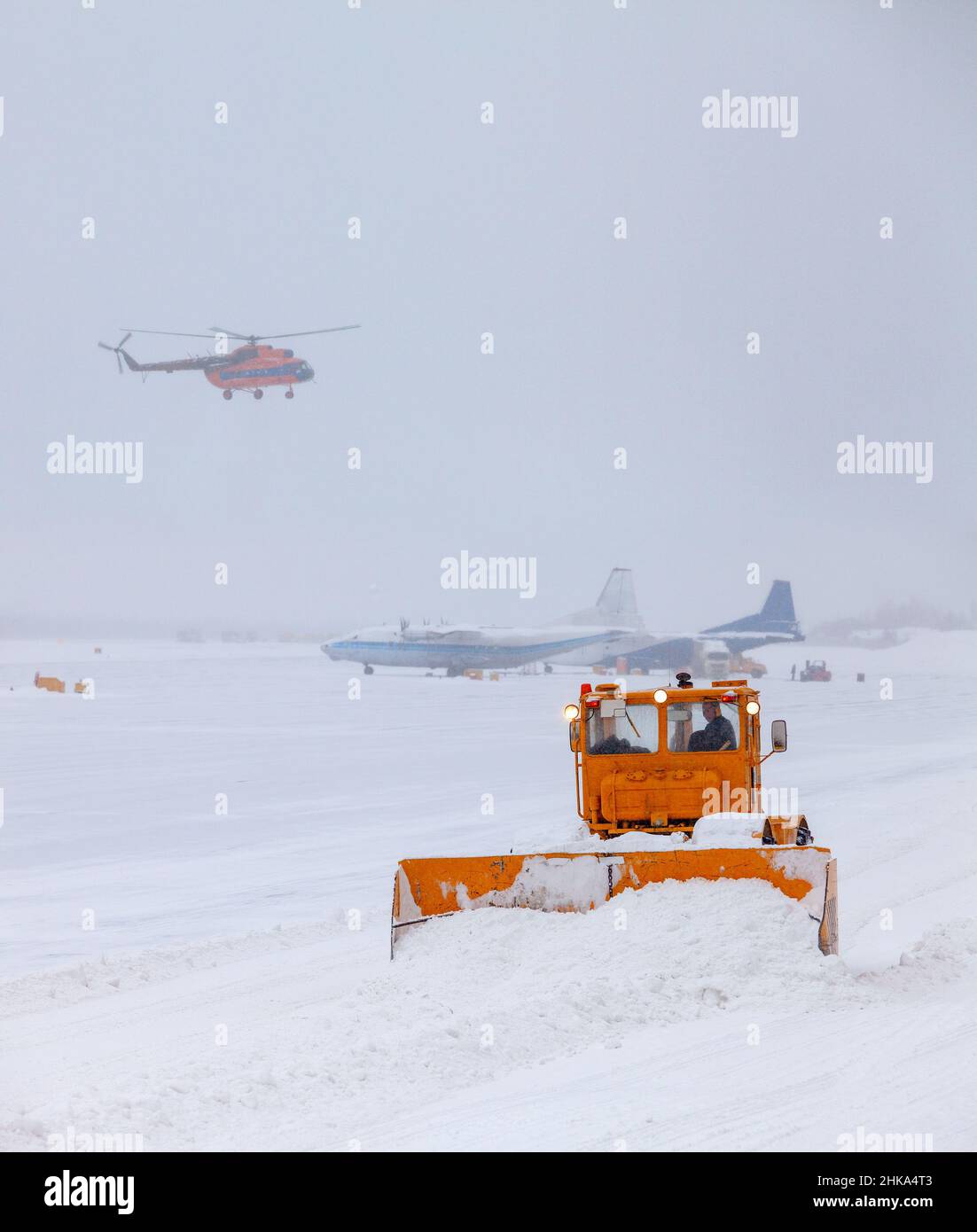 L'aratro da neve pulisce la pista dopo una forte tempesta di neve. L'elicottero sta atterrando in cattive condizioni meteorologiche, durante una nevicata pesante. La trasp Foto Stock L'aratro da neve pulisce la pista dopo una forte tempesta di neve. L'elicottero sta atterrando in cattive condizioni meteorologiche, durante una nevicata pesante. La trasp Foto Stock
