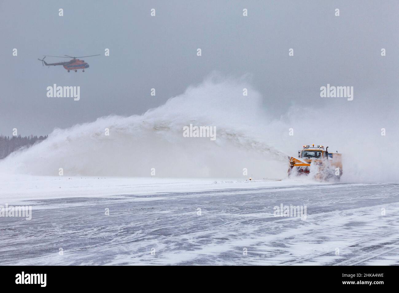 L'aratro da neve pulisce la pista dopo una forte tempesta di neve. L'elicottero sta atterrando in cattive condizioni meteorologiche, durante una nevicata pesante. Foto Stock L'aratro da neve pulisce la pista dopo una forte tempesta di neve. L'elicottero sta atterrando in cattive condizioni meteorologiche, durante una nevicata pesante. Foto Stock