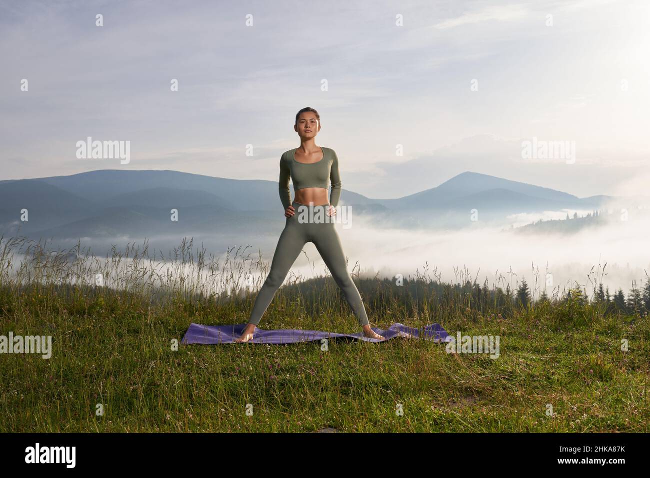 Vista frontale di una donna atletica che fa posa di triangolo da yoga e guarda la macchina fotografica. Attraente femmina hanno mattina esercizio all'aperto, mantenendo asana. Concetto di salute. Foto Stock