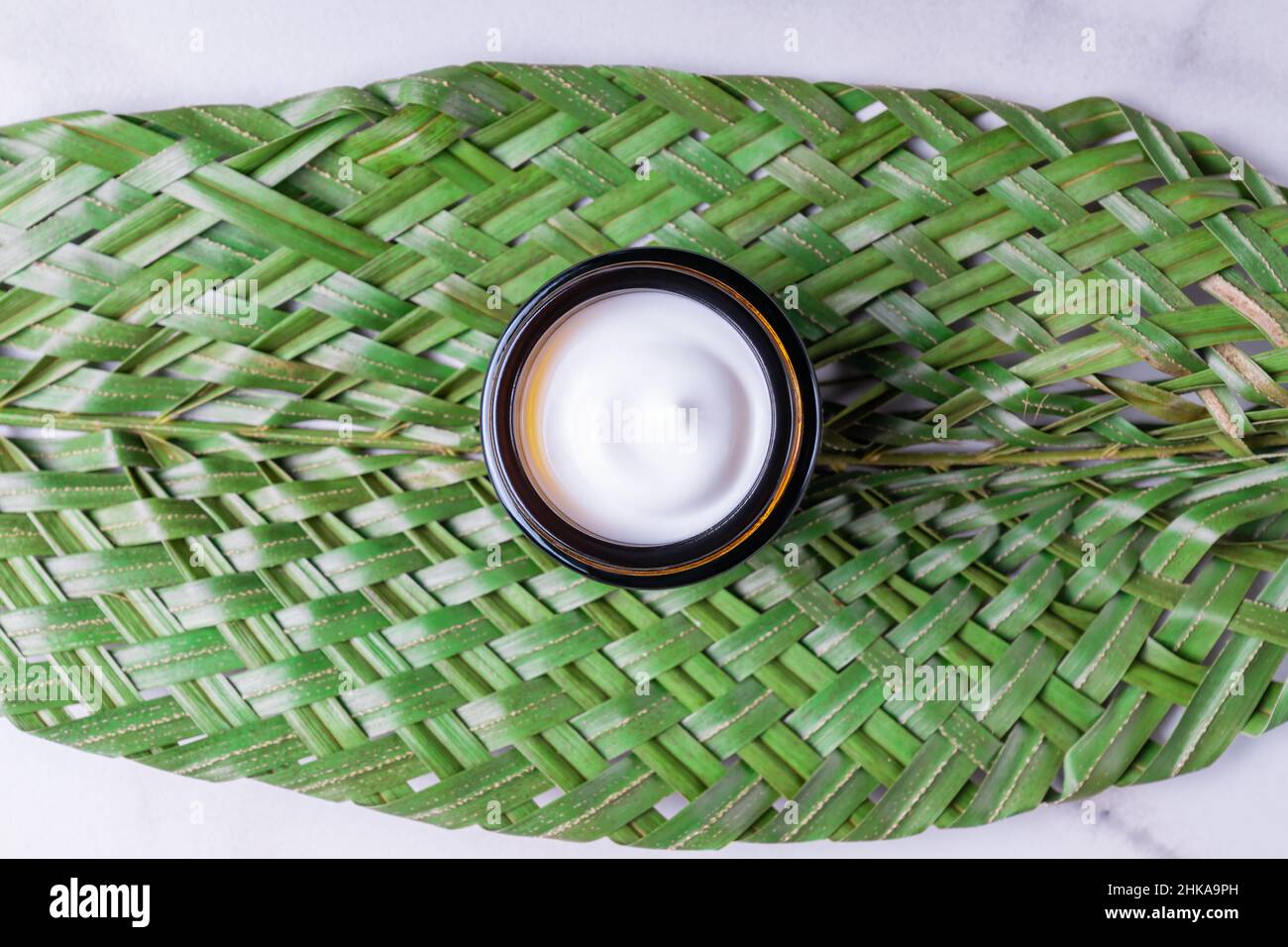 Vaso in vetro ambrato di crema idratante su sfondo verde foglia. Marchio naturale ecologico del prodotto di bellezza, design di imballaggio Foto Stock