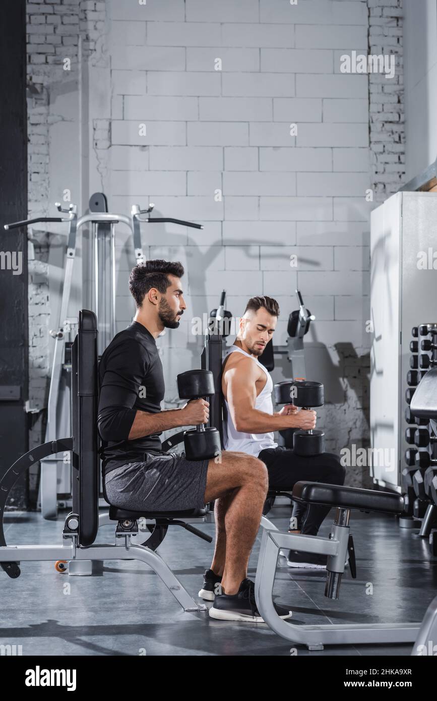 Giovani sportivi interrazziali che si allenano con manubri e attrezzature sportive in palestra Foto Stock